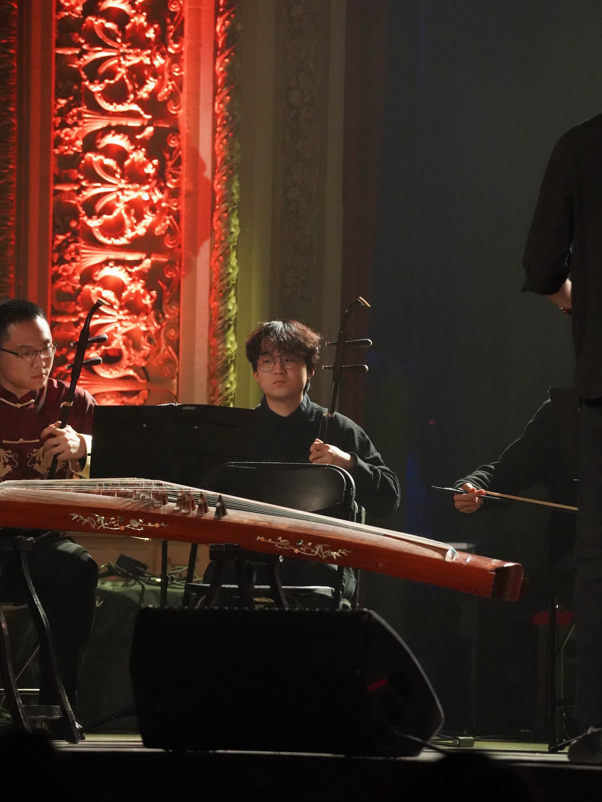 A guzheng player beside a carved red pillar
